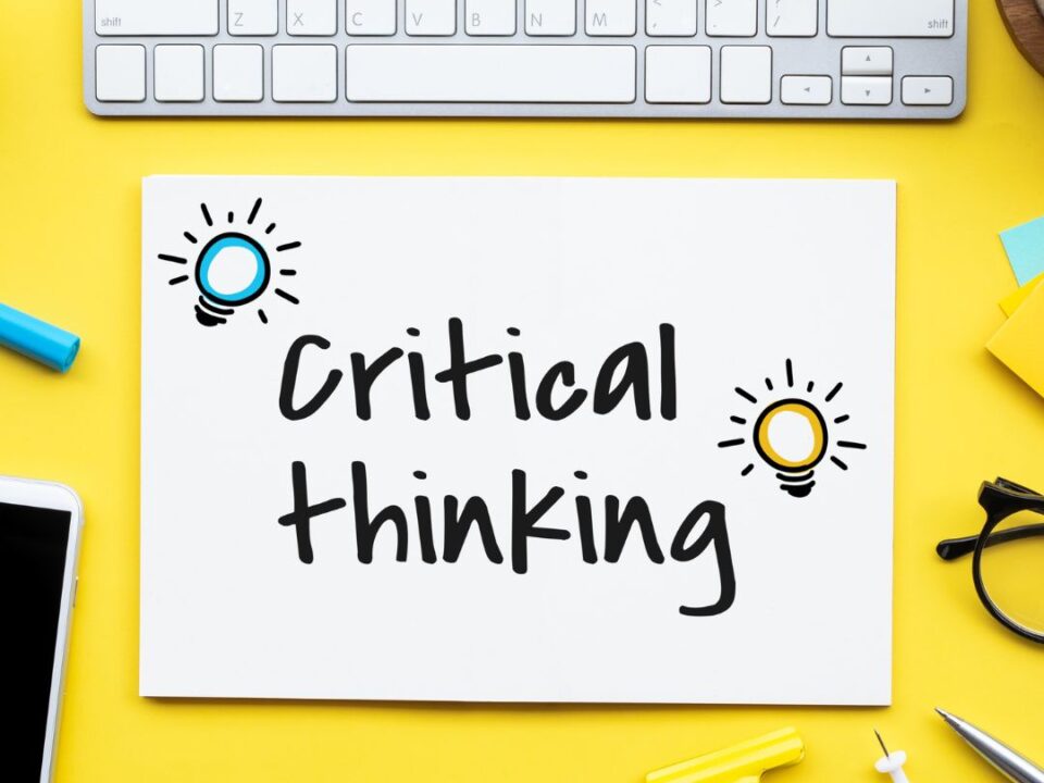 Critical Thinking words written on a piece of paper on a yellow background with a keyboard in the image